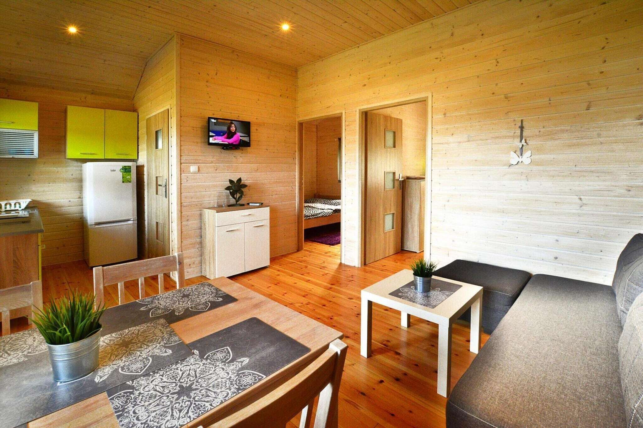 A compact wooden cabin with a dining area, a sofa, a small table, and a TV in the living room.