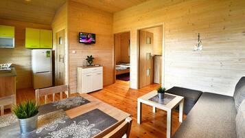A compact wooden cabin with a dining area, a sofa, a small table, and a TV in the living room.