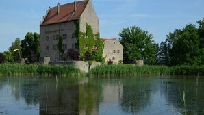A large stone building with a red roof, surrounded by a calm body of water and greenery. - Ferienwohnung am Kummerower See, Sommersdorf (Sommersdorf)
