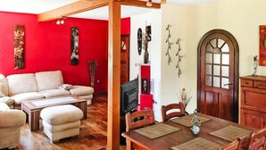 A living room with a red wall, a beige sofa, a wooden dining table, and a fireplace. - Ferienwohnung am Kummerower See, Sommersdorf (Sommersdorf)