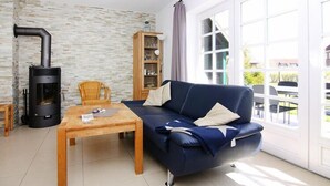 A living room with a sofa, a table, a bookshelf, and a wood-burning stove. - Ferienwohnung im Reihenhaus, Friedrichkoog-Spitze (Friedrichskoog-Spitze)