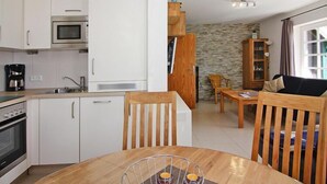 A compact kitchen with white cabinets, a microwave, and a coffee maker. There is a dining area with a wooden table and chairs. - Ferienwohnung im Reihenhaus, Friedrichkoog-Spitze (Friedrichskoog-Spitze)
