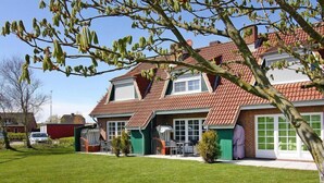 A two-story house with a red-tiled roof, a green garage, and a well-maintained lawn. - Ferienwohnung im Reihenhaus, Friedrichkoog-Spitze (Friedrichskoog-Spitze)