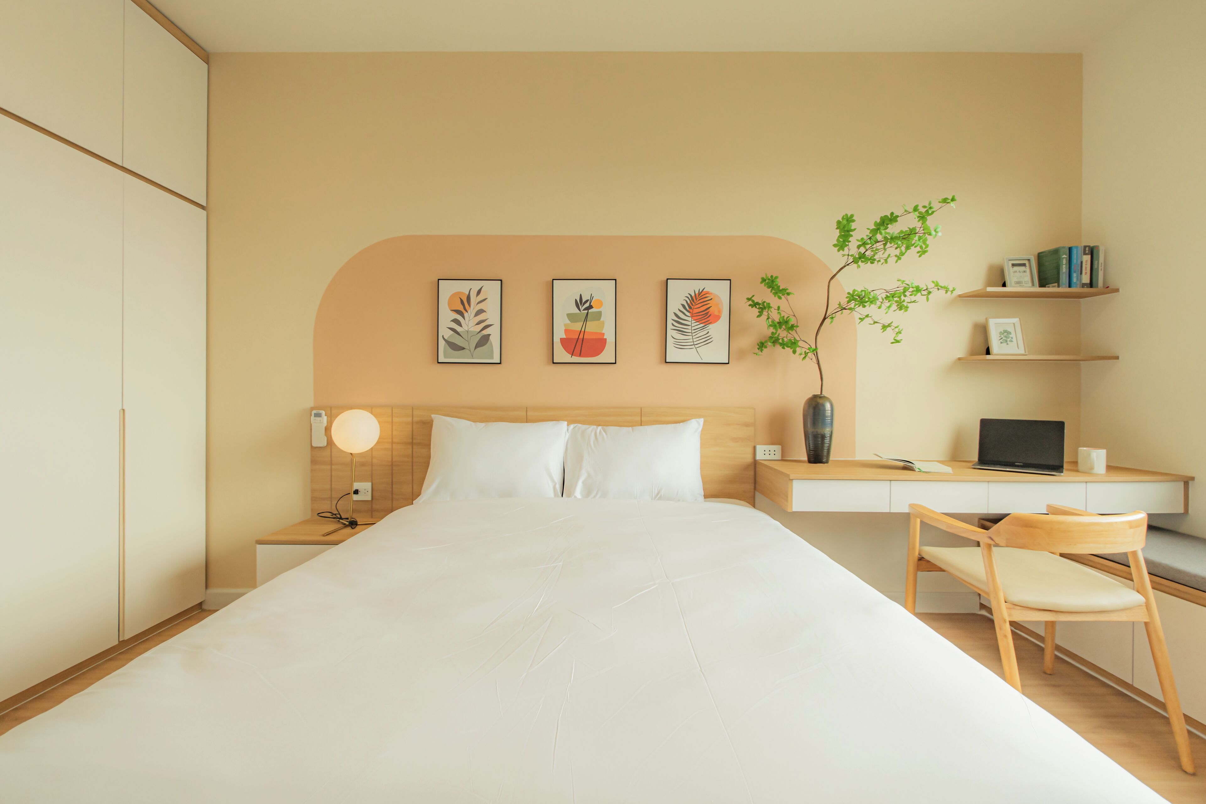 Habitació d'hotel moderna amb un llit gran, un escriptori amb un ordinador portàtil i una petita biblioteca.