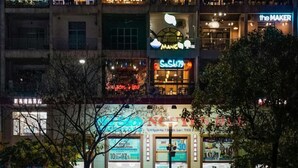 Un immeuble à plusieurs étages, orné de divers panneaux lumineux indiquant différents commerces, notamment des cafés et des restaurants.