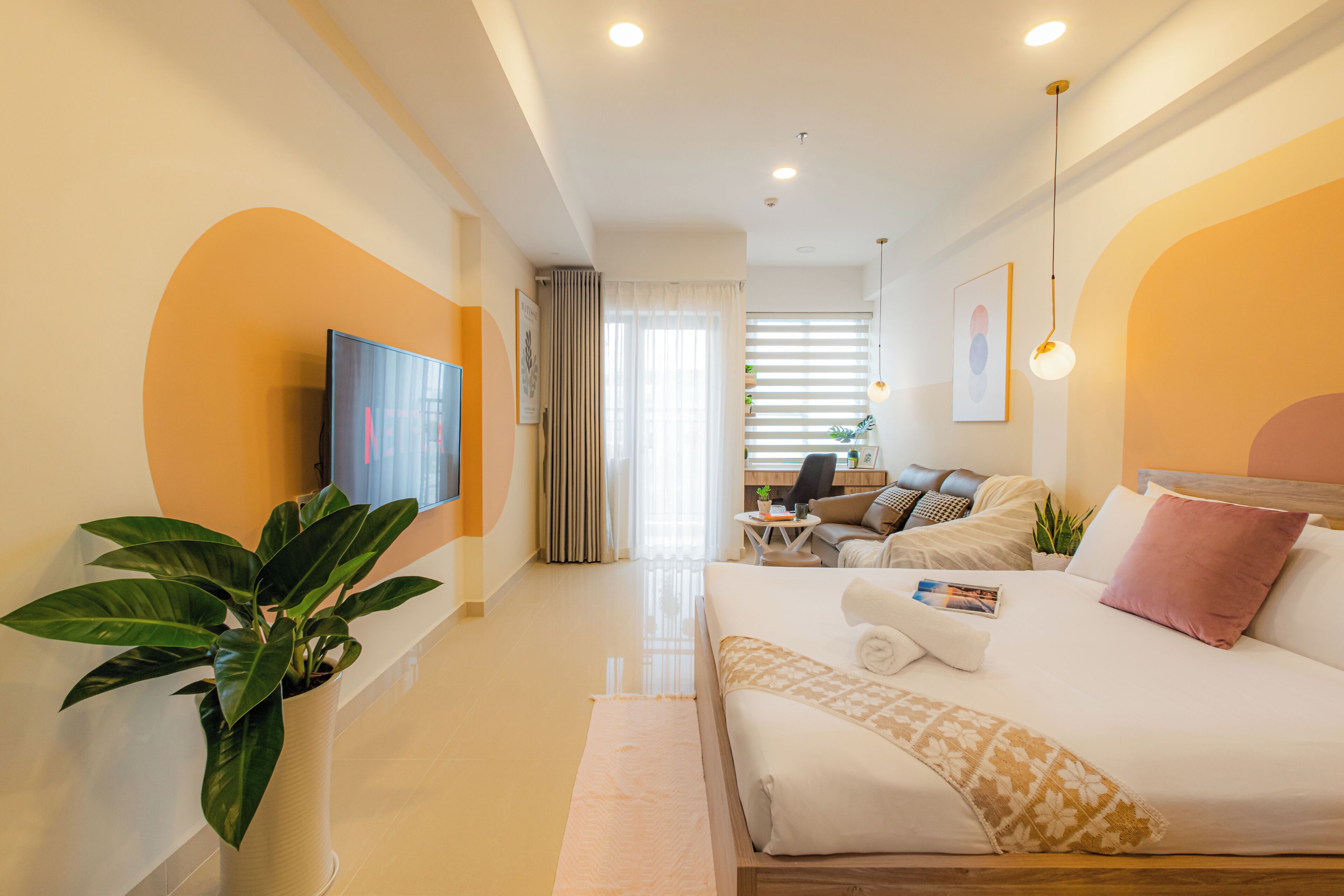 Una habitación de hotel moderna con una cama grande, un televisor, un escritorio con una silla y una planta en maceta.