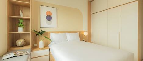 A modern bedroom with a large bed, a bedside table with a lamp, a shelf with decorative items, and a wall-mounted artwork.