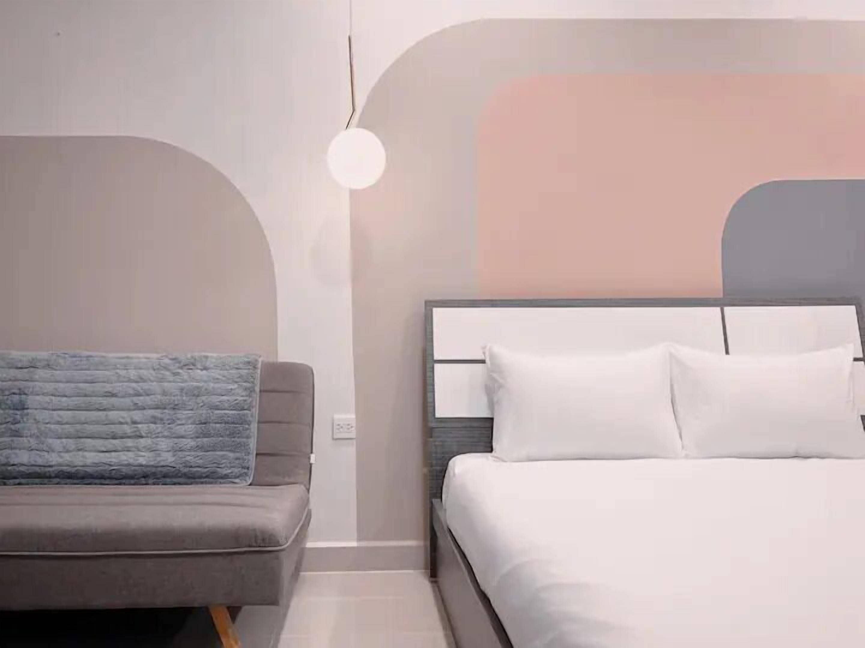 A modern bedroom with a grey sofa, a white bed, and a unique wall design.