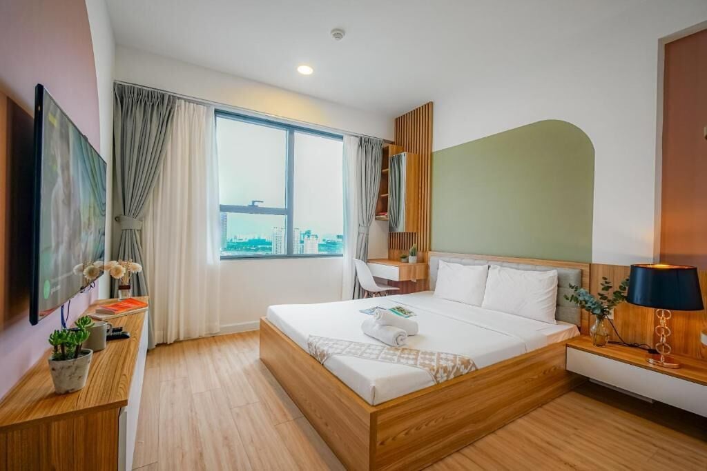 A modern hotel room with a large bed, a desk, a chair, and a window with a city view.