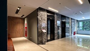 Un hall d’entrée moderne avec un comptoir de réception en marbre, des ascenseurs et un extincteur.