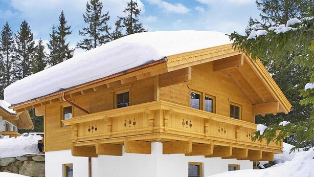 Een houten chalet met balkon, omgeven door sneeuw en bomen.