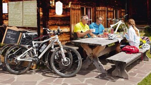 Een houten terras met een eettafel en banken, een fiets en een menubord.