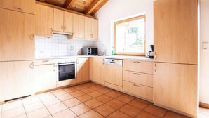 Een keuken met houten kastjes, een betegelde spatwand, een raam en een betegelde vloer.