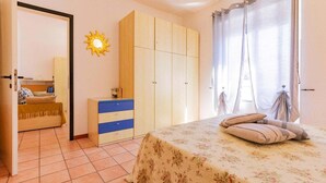 Une chambre à coucher comprenant un lit, une armoire, un petit meuble, un miroir et un motif décoratif représentant un soleil sur le mur.