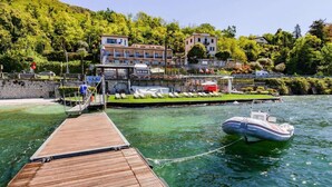 Une jetée en bois s’avance sur un lac, et un bateau y est amarré. Au fond, on aperçoit des bâtiments dotés de balcons donnant sur l’eau.