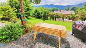 A wooden bench in a garden with a gravel path, surrounded by greenery and a distant view of a house and mountains. - Wellness- Hottub & Sauna- Pet Friendly- Hiking (Keutschach am See)