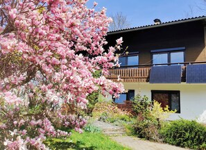 A modern two-story house with a balcony, surrounded by lush greenery and blooming pink flowers. - Wellness- Hottub & Sauna- Pet Friendly- Hiking (Keutschach am See)