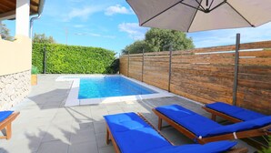 A swimming pool with lounge chairs and an umbrella.