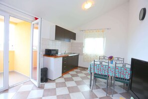 A compact kitchen with a microwave, sink, and cabinets, a dining table with chairs, and a sliding glass door leading to an outdoor area.