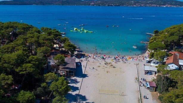 An aerial view of a beach with clear blue water, boats, and people.