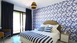 Ein Schlafzimmer mit einem großen Bett, einem Rattan-Kopfstück, einem Nachttisch und einem Sessel.