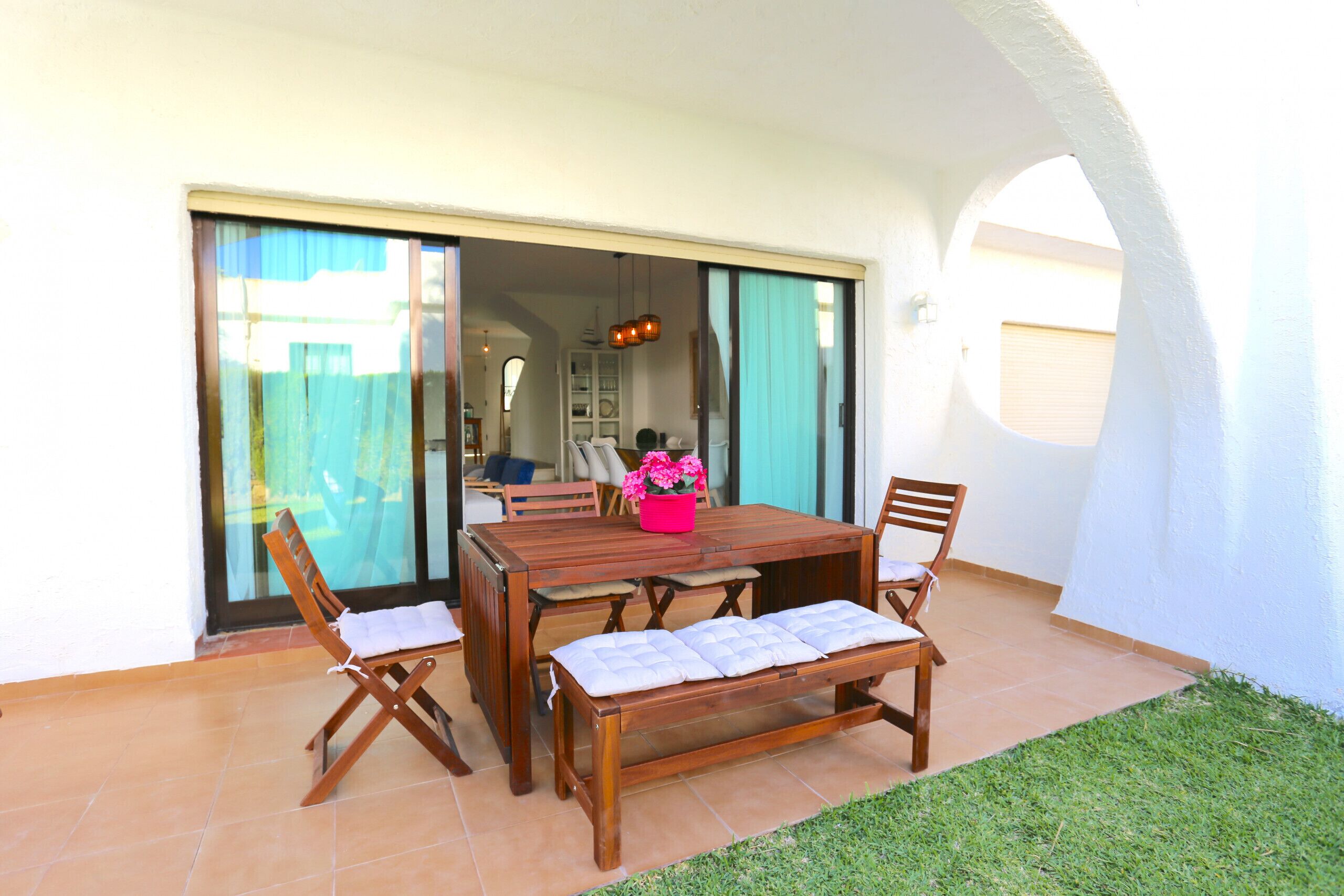 An outdoor patio with a wooden table and chairs, a bench, and a small garden area.