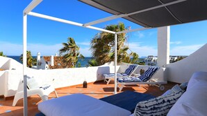 Eine Dachterrasse mit weißen Wänden, blau gestreiften Liegestühlen und einem Bett mit gemusterten Kissen.