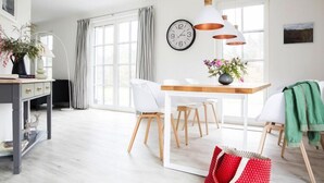 Ein modernes Wohnzimmer mit Essbereich, großen Fenstern und einer Wanduhr.