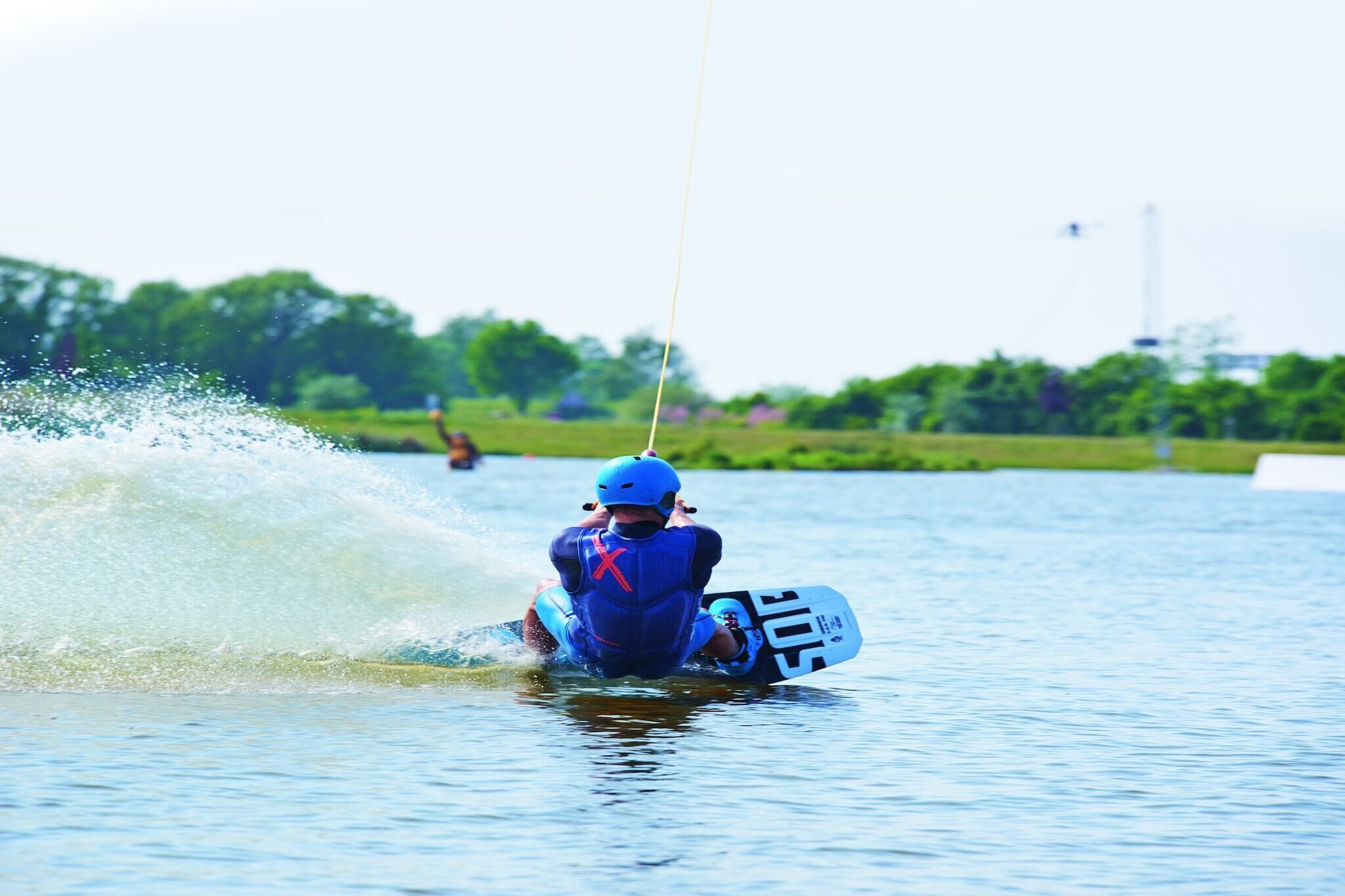 A person wakeboarding on a body of water with a clear sky and greenery in the background.