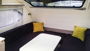 Interior compacto de una caravana con sofá, una mesita y una ventana con persianas, con vistas al exterior.