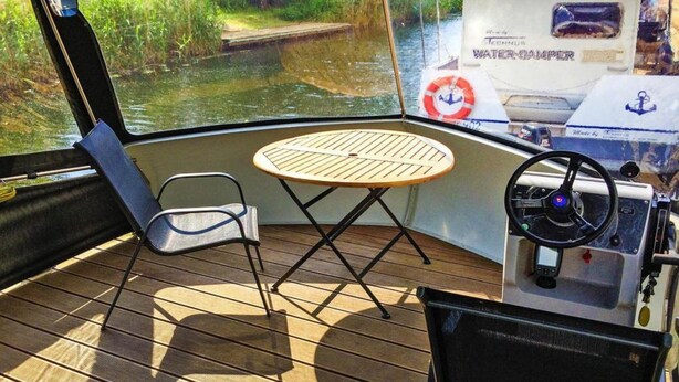 Interior de un barco con timón, una mesa y una silla.
