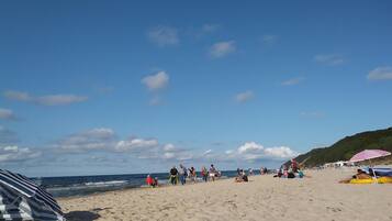 A beach with people walking and sitting, a clear sky, and a sandy shore.
