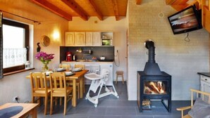 Eine gemütliche Küche mit Holzausbau, einem Esstisch mit Stühlen und einem Hochstuhl für Babys, sowie einem schwarzen Kaminofen.