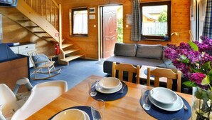 Ein gemütliches Blockhaushaus-Interieur mit einer Holztreppe, einer Couch, einem Esstisch für vier Personen und einem an der Wand montierten Fernseher.