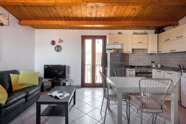 Un espacio habitable compacto con sofá, televisor, mesa de comedor, sillas, área de cocina y piso de baldosas.