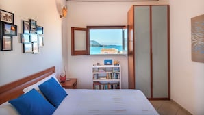 A bedroom with a bed, a bookshelf, a wardrobe, and a window with a view of the sea. - Terrazza Mandralisca by Wonderful Italy (Cefalù)