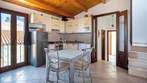 A modern kitchen with wooden ceiling beams, white cabinets, a stainless steel refrigerator, and a dining table with metal chairs. - Terrazza Mandralisca by Wonderful Italy (Cefalù)