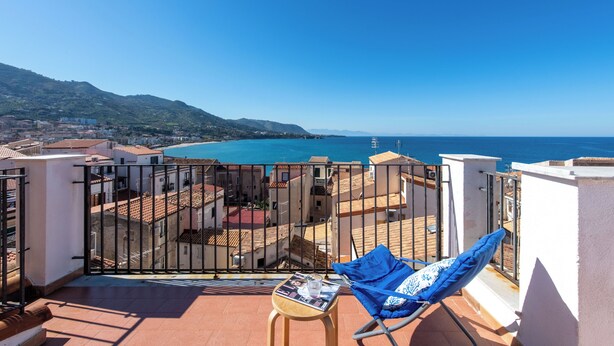 A balcony with a view of the sea, a chair, and a small table with a magazine. - Terrazza Mandralisca by Wonderful Italy (Cefalù)