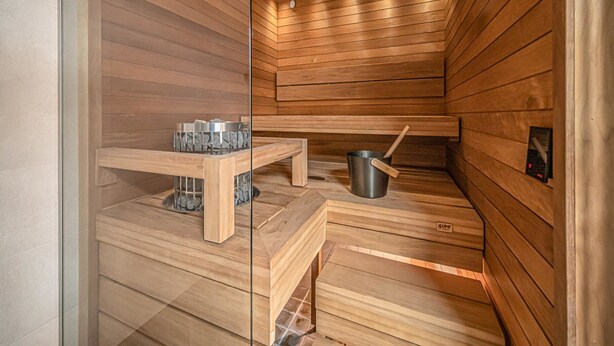Sauna, jossa on puuseinät ja -lauteet, metallinen ämpäri ja lasiseinä.