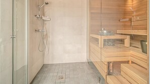 Moderni kylpyhuone, jossa on lasinen suihkuseinä, puiset saunapenkit ja laatoitettu lattia.