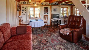 Uma sala de estar acolhedora com carpete estampado, uma poltrona de couro marrom, um sofá vermelho, uma mesa de jantar com toalha branca e uma televisão.