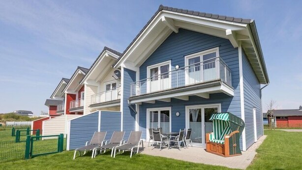 A two-story house with a balcony, a covered patio with chairs, and a fenced yard. - Luxuriös eingerichtetes Ferienhaus in Strandnähe (Dagebüll)