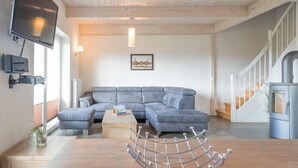 A modern living room with a sectional sofa, a wooden coffee table, and a TV mounted on the wall. - Luxuriös eingerichtetes Ferienhaus in Strandnähe (Dagebüll)