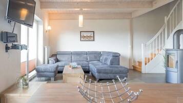 Ein modernes Wohnzimmer mit einer Eckcouch, einem Couchtisch aus Holz und einem an der Wand montierten Fernseher.