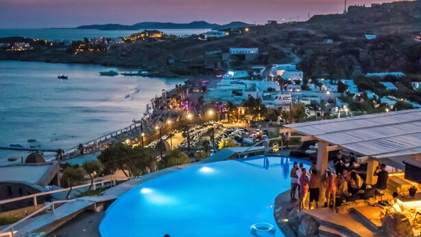 Ein Resort mit großem Pool, Sitzgelegenheiten im Freien und Blick auf das Meer und die Stadt im Abenddämmerung.