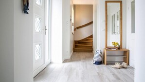 Un couloir avec un escalier en bois, un miroir et un banc sur lequel sont posées des chaussures.