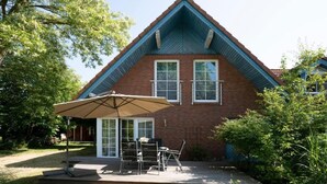 A two-story brick house with a gabled roof, a patio with outdoor furniture, and a large umbrella.