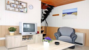 A living room with a television, a grey armchair, a wooden coffee table, a small plant, and a painting of a beach scene.
