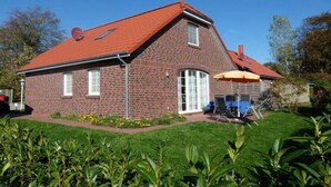 A brick house with a red roof, a covered patio, and a lawn.