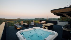 Een terras op het dak met een jacuzzi, tuinmeubilair en uitzicht op het landschap.